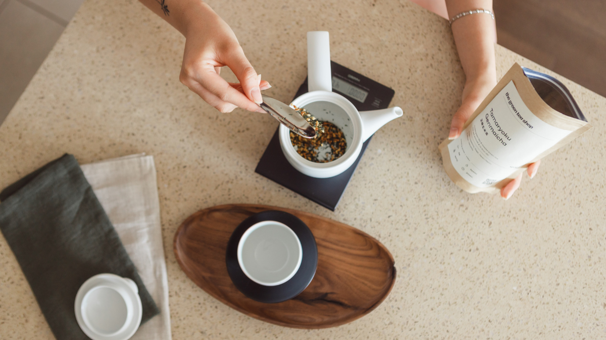 Person preparing tea with a teapot and tea leaves on a scale.